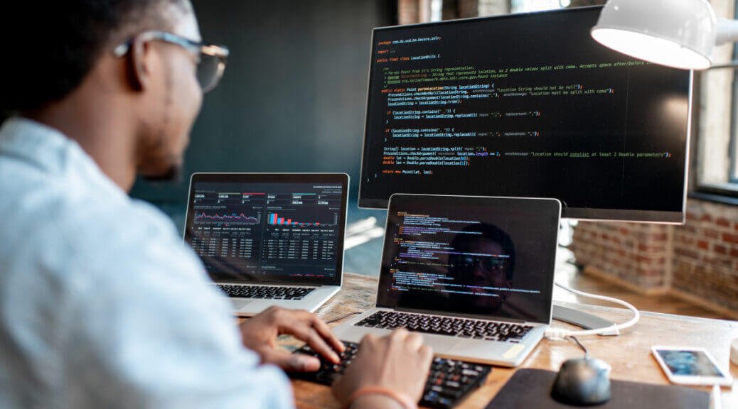 programmer working on two laptop and three screens